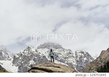 asian man standing on top of rock looking at peak of snow mountain 129751645