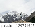 asian man standing on top of rock looking at peak of snow mountain 129751647