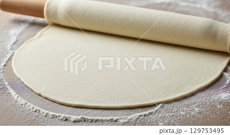 Rolling dough with wooden rolling pin on floured surface for baking 129753495