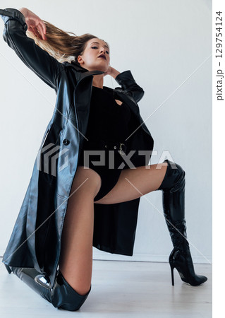 woman in black leather raincoat and latex boots 129754124