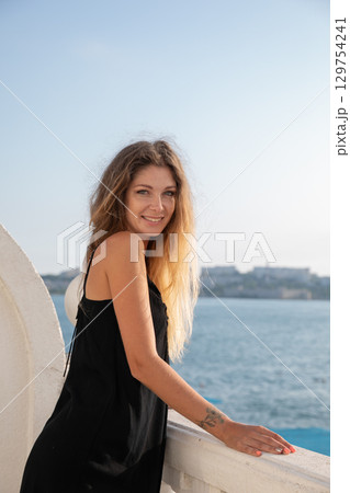 Blonde in a black dress walking on the beach by the sea Blonde in a black dress walking on the beach by the sea 129754241