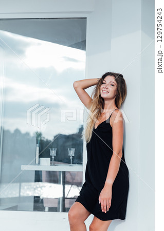 Slim blonde woman in black summer dress smiling 129754243