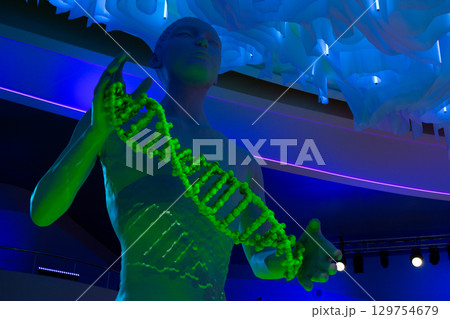 Futuristic sculpture depicting human figure holding glowing green DNA helix, symbolizing the concept of new life and genetic evolution, illuminated by blue neon lights 129754679