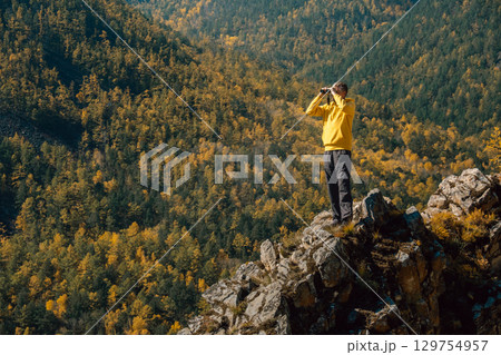 hiker stands on rocky outcrop, enjoying stunning views vibrant autumn foliage and distant mountains. 129754957