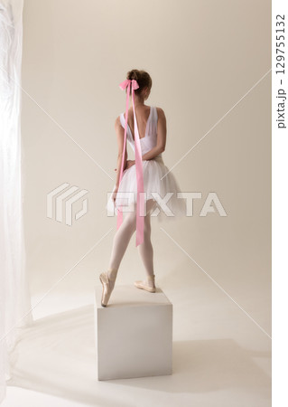 Ballerina with long pink ribbon bow in white tutu balancing on pointe Ballerina with long pink ribbon bow in white tutu balancing on pointe 129755132