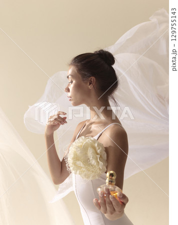 Elegant woman with floral accessory holding perfume bottle Elegant woman with floral accessory holding perfume bottle 129755143