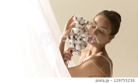 The bloom inside her. Woman with cotton bouquet touching face in serene beauty portrait 129755238