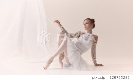 Graceful ballerina in white costume seated elegantly on pointe shoes 129755285