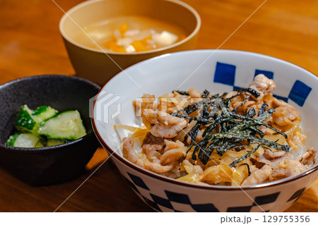 鶏肉と玉ねぎの丼ぶりに味噌汁と漬物を添えた和風夕食セット 129755356