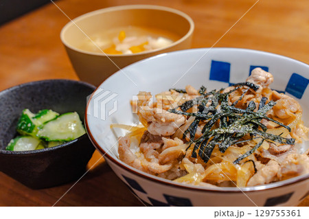 鶏肉と玉ねぎの丼ぶりに味噌汁と漬物を添えた和風夕食セット 129755361