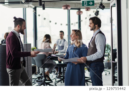 Collegues talking about project document, standing in modern office. 129755442