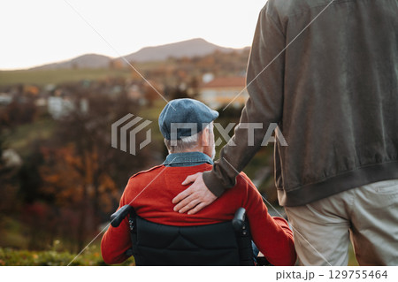 Grandson standing behind his older grandad in wheelchair, enjoying view. 129755464