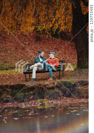 Son and older father sitting on bench by lake and talking. 129755493