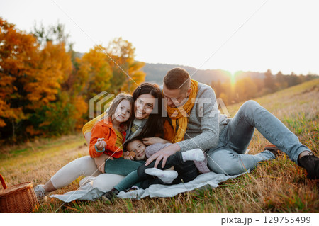 Parents with young children sitting outdoors in autumn light. 129755499