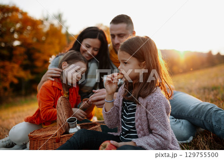 Parents with young children sitting outdoors in autumn light. 129755500