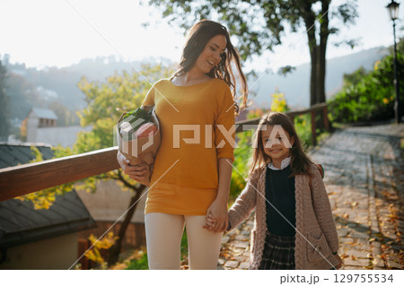 Mother and daughter going home after school, carrying shopping bag. 129755534