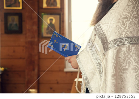 A priest holds a book for reading prayers during the rite of baptism in the Orthodox Church. Inscription on the book: the rite of baptism 129755555