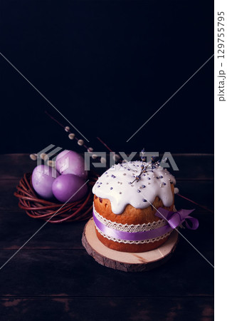 Easter cakes on a dark background, decorated with lavender and marshmallows, and painted Easter eggs in a wicker nest Easter cakes on a dark background, decorated with lavender and marshmallows, and painted Easter eggs in a wicker nest 129755795