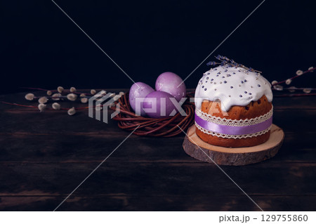 Easter cakes on a dark background, decorated with lavender and marshmallows, and painted Easter eggs in a wicker nest Easter cakes on a dark background, decorated with lavender and marshmallows, and painted Easter eggs in a wicker nest 129755860