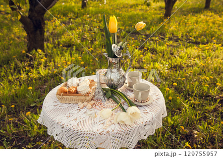 Romantic picnic in the spring blooming Apple orchard. A coffee table with cups, candy, pastries, and a vase of tulips. Romantic picnic in the spring blooming Apple orchard. A coffee table with cups, candy, pastries, and a vase of tulips. 129755957