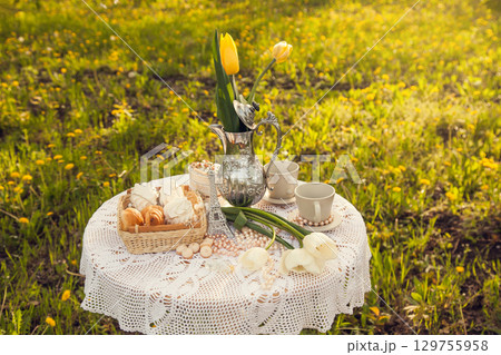 Romantic picnic in the spring blooming Apple orchard. A coffee table with cups, candy, pastries, and a vase of tulips. Romantic picnic in the spring blooming Apple orchard. A coffee table with cups, candy, pastries, and a vase of tulips. 129755958