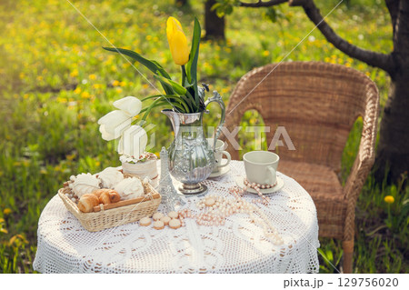 Romantic picnic in the spring blooming Apple orchard. A coffee table with cups, candy, pastries, and a vase of tulips. 129756020