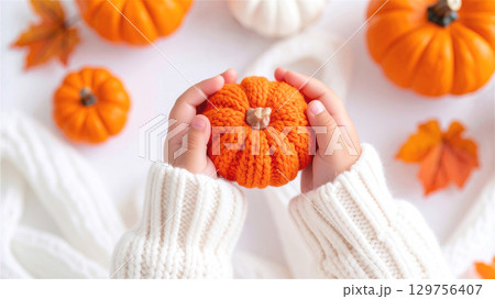 ニットのハロウィンかぼちゃを持っている小さな子供の両手 129756407
