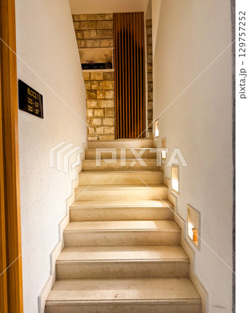 A stone staircase with warm side lights leads to the upper floor inside the building. Perspective, hospitality and interior design expressed through modern architectural detail. A stone staircase with warm side lights leads to the upper floor inside the building. Perspective, hospitality and interior design expressed through modern architectural detail. 129757252