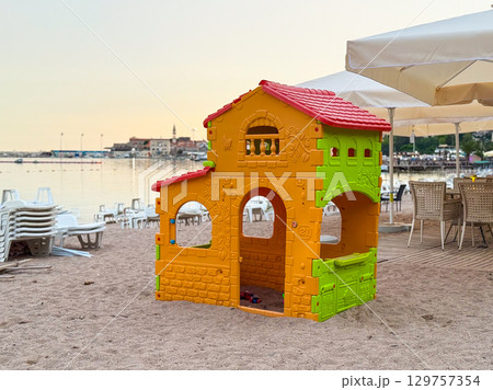 A colorful toy house for children standing on the sandy beach near the sea. Childhood, family leisure and playful seaside vacation atmosphere with imagination. 129757354