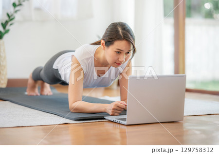 Asian woman doing plank exercise at home with laptop 129758312
