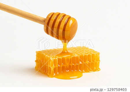 Golden honey dripping from a wooden dipper onto fresh honeycomb isolated on white background. concept of natural sweetener, organic food, beekeeping, culinary ingredient. 129758403