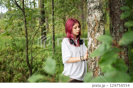 Young girl with pink hair exploring forest and touching tree trunk Young girl with pink hair exploring forest and touching tree trunk 129758554