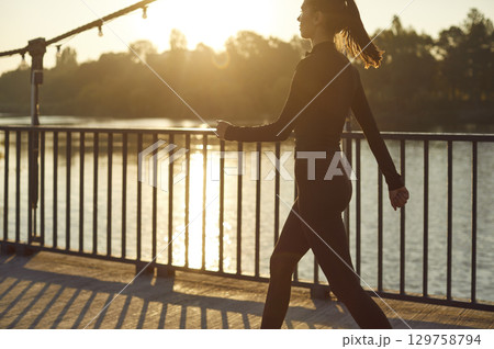 Beautiful sporty young woman walking on city bridge after outdoor fitness workout Beautiful sporty young woman walking on city bridge after outdoor fitness workout 129758794