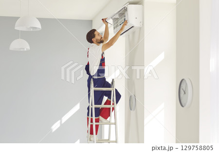 Male professional worker repairs air conditioner and cleans filters in client's apartment. Male professional worker repairs air conditioner and cleans filters in client's apartment. 129758805