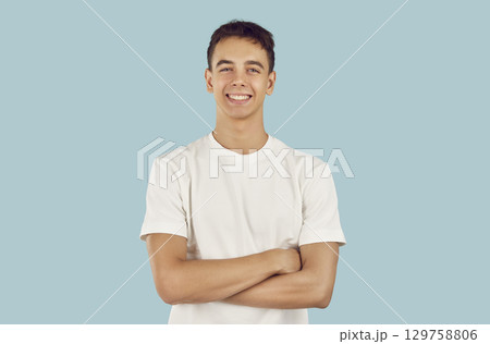 Portrait of happy, cheerful young man or teenage boy with folded arms on blue background 129758806