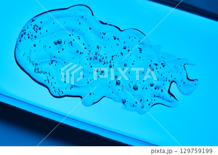 The texture of the serum is in the form of a drop on a blue background. 129759199
