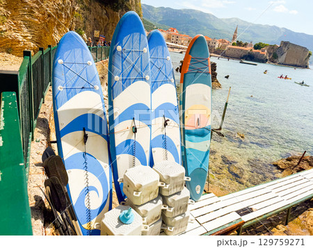 Surfboards with paddles placed by the sea with town and mountains in background. Adventure, recreation, summer lifestyle and coastal tourism in seaside travel scene. 129759271