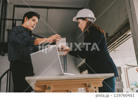 Construction manager and engineer dressed in orange work vests and hard helmets explore construction documentation on the building site near the steel frames 129760481