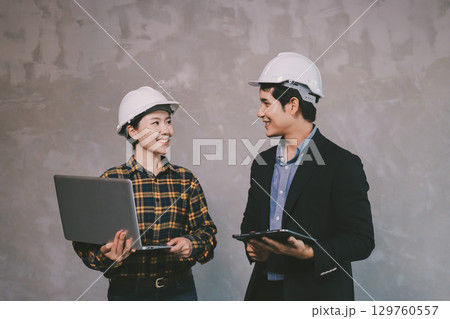 Construction manager and engineer dressed in orange work vests and hard helmets explore construction documentation on the building site near the steel frames 129760557