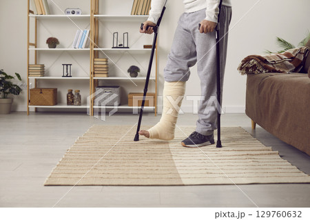 Handicapped young man with broken leg trying to walk with crutches. 129760632