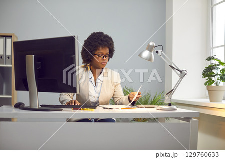 Serious, focused young beautiful African American woman with glasses, dressed in white blouse and business suit. Serious, focused young beautiful African American woman with glasses, dressed in white blouse and business suit. 129760633