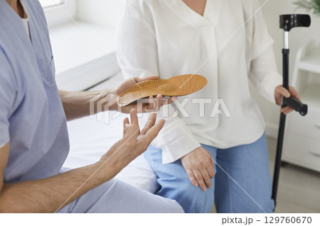 Doctor podiatrist gives medical orthotic insoles to a woman patient with a foot injury 129760670