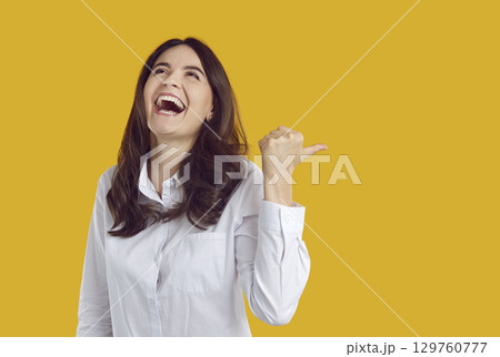 Happy laughing young woman pointing to side with thumb up 129760777