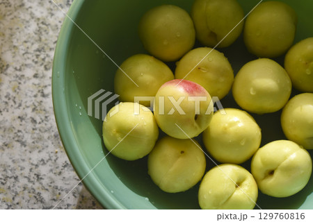 A ripe yellow plum in a green basin. Juicy fruit. Ripe plums in drops of water. 129760816