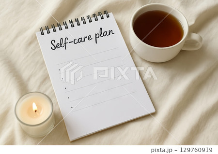 Cozy self-care scene with a blank notepad, hot cup of tea, and candle on a soft fabric surface. concept of self-care, relaxation, personal wellness planning. 129760919