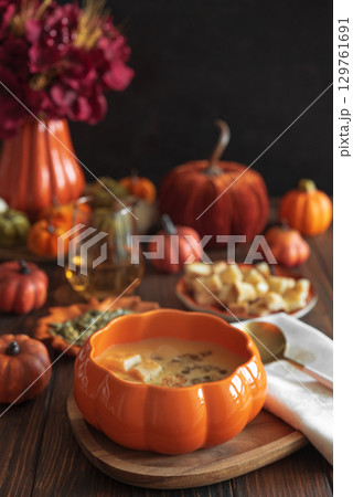 Creamy pumpkin soup with croutons and seeds, served in a pumpkin-shaped bowl on dark wooden table. 129761691