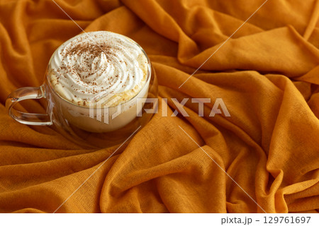 Cozy pumpkin latte with whipped cream and spices on an orange fabric background. Cozy pumpkin latte with whipped cream and spices on an orange fabric background. 129761697