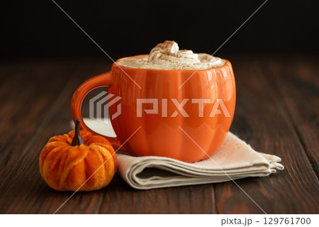 Cozy pumpkin latte in a pumpkin-shaped mug with whipped cream and spices, surrounded by autumn decor. Cozy pumpkin latte in a pumpkin-shaped mug with whipped cream and spices, surrounded by autumn decor. 129761700