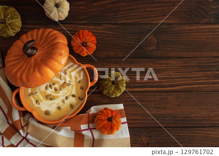 Autumnal lunch with pumpkin soup in a pumpkin-shaped bowl, croutons and festive decor on dark wooden table. Top view 129761702