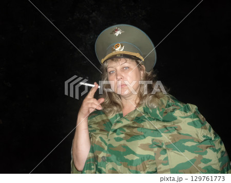 Beautiful middle-aged woman in Russian military uniform poses for the camera with a cigarette in her hand. Beautiful middle-aged woman in Russian military uniform poses for the camera with a cigarette in her hand. 129761773